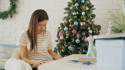 A girl is reading a book while sitting at a table near the Christmas tree. Stock Footage 103534977