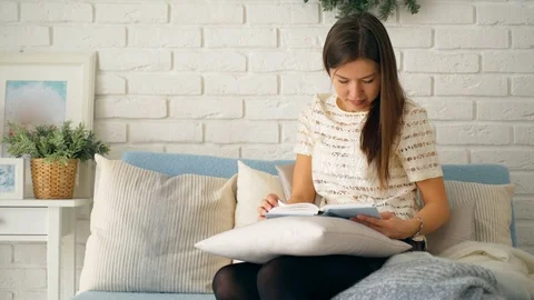 A girl is reading a book while sitting on a blue sofa. Stock Footage 106453384