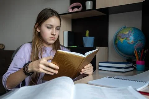 Girl reading book while sitting at table, preparing for school. Educational.. 스톡 사진