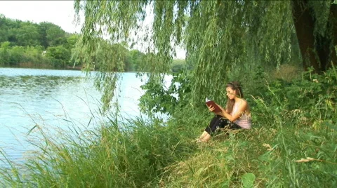 Girl reads the book on the bank of river Stock Footage
