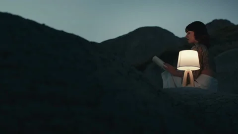 Girl reads a book on how to develop imagination on a rock Stock Footage 213970725