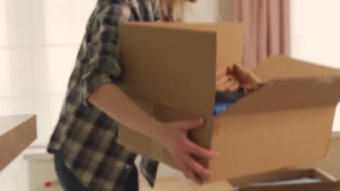 The girl rearranges the open box for moving to the floor. Stock Footage
