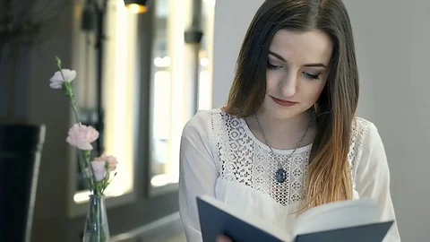 Girl receives message on smartphone while reading book in the cafe, steadycam  Stock Footage 73510652