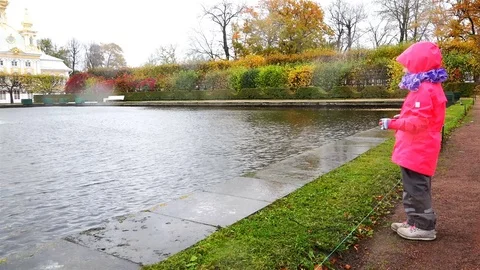A girl in a red jacket is standing in the rain near the shore of a pond Stock Footage