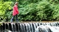 Girl in red jacket walks along small overflow dam on the river in the forest HD Footage