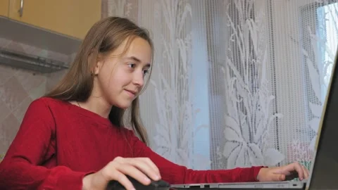 A girl in a red sweater plays video games on a laptop while sitting on a chair Video stock 211383353