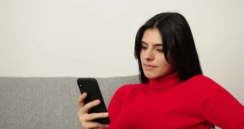 Girl relaxing on couch using smart phone in house. Happy brunette write sms Stock-Footage 120609119