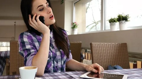 Girl in the restaurant using tablet pc and answering the phone. She is sad Stock Footage 61408998