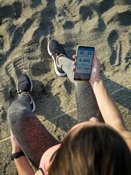 Girl resting after running while watching running app on mobile phone. Stock Photos