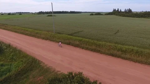 Girl riding a bicycle on a red sand rural road panoramic Stock Footage