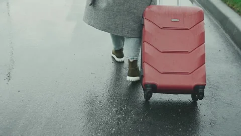 A girl in a road coat pulls a red suitcase on wheels on wet asphalt in the rain. Stock Footage 132255257