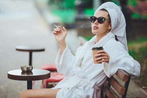 A girl in a robe drinks coffee and smokes a cigarette Stock Photos