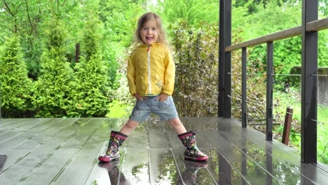 A girl in rubber boots splashes through the puddles on the terrace. Stock Footage 155339802
