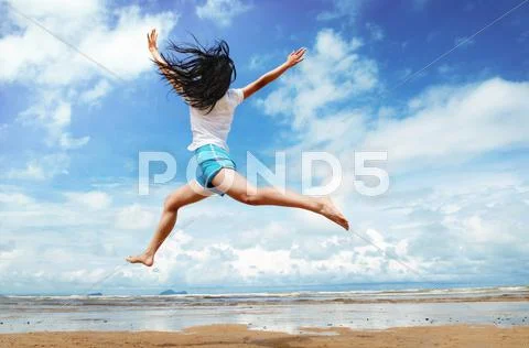 Girl On A Sandy Beach By The Ocean, Jumping In The Air.