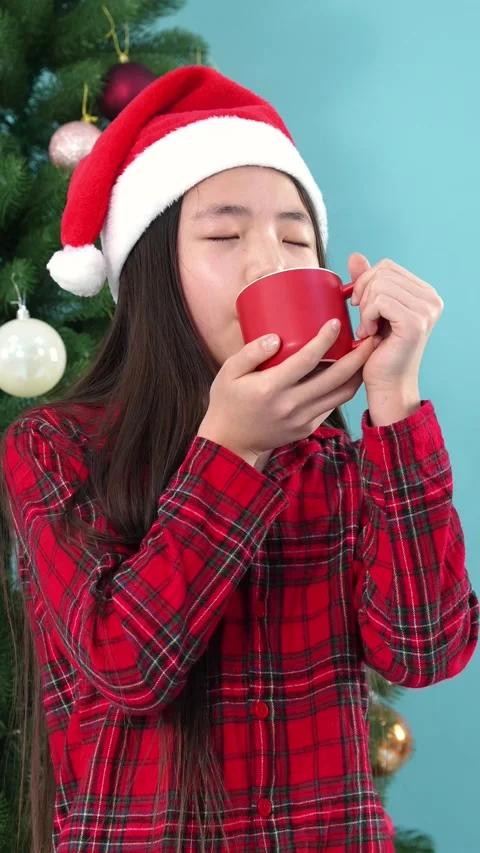 Girl in Santa Hat Drinking Hot Chocolate near Christmas Tree Stockbeeldmateriaal 346229751