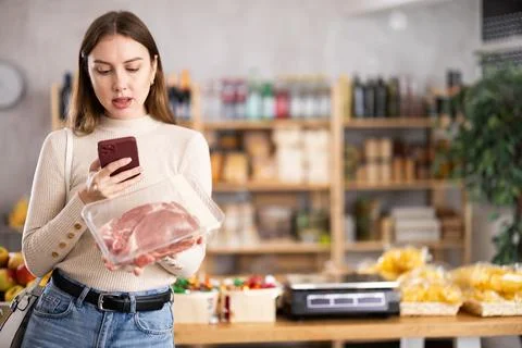 Girl scan QR-code on raw pork package in store Stock-Fotos