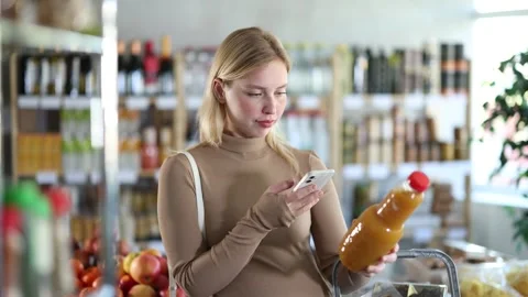 Girl scan QR code, take reading peach juice label using phone camera in shop Stock Footage 310276711