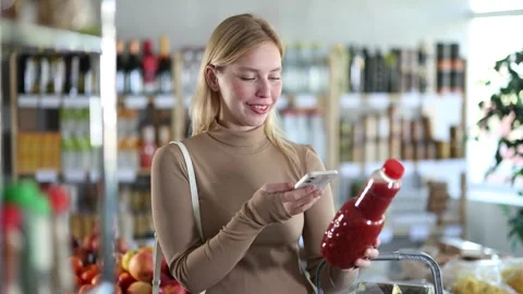 Girl scan QR code, take reading tomato juice label using phone camera in shop Stock Footage 310317399