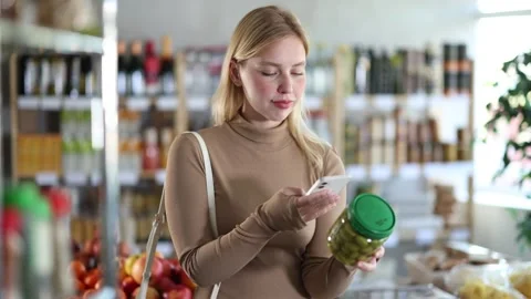 Girl scan QR code, take reading pickled olives label using phone camera in shop Stock Footage 310529425