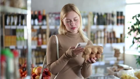 Girl scan QR code, take reading eggs label using phone camera in shop Stock Footage 311351274