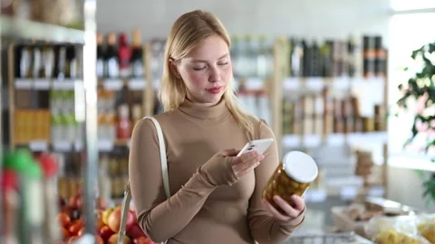 Girl scan QR code, take reading pickled olives label using phone camera in shop Stock Footage 343711075