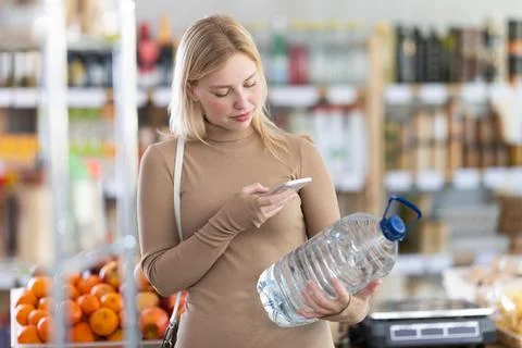 Girl scan QR code, take reading drinking water label using phone camera in shop Stock-Fotos