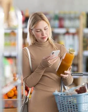 Girl scan QR code, take reading peach juice label using phone camera in shop Foto stock