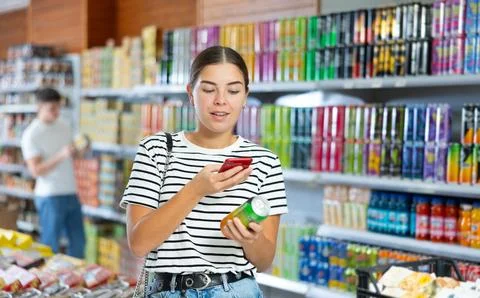 Girl scanning QR code on can of soft drink with smartphone in grocery store Stock-Fotos