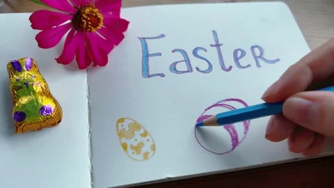 Girl scribbling EASTER using her color pencils and sketchbook. A chocolate bunny Stock Footage 171013850