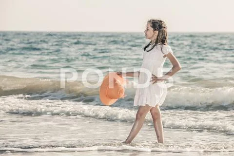 Girl on the seashore wearing an orange hat and a white dress Stock Photos