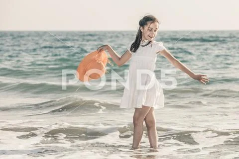Girl on the seashore wearing an orange hat and a white dress Stock Photos