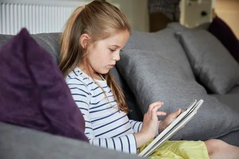 A girl seated looking at a digital table, using the touch screen. Stock Photos