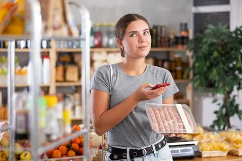 Girl shopper scanning QR code on raw sausages label in grocery department of Stockfoto's