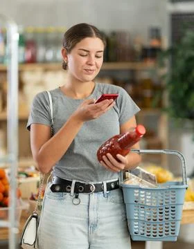 Girl shopper scanning QR code on bottle tomato juice label in grocery department Stockfoto's