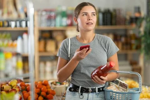 Girl shopper scanning QR code on bottle tomato juice label in grocery department Foto stock