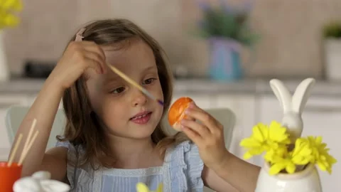A girl shows a decorated egg for the Easter holiday, sitting at a table Stock-Footage 233598656