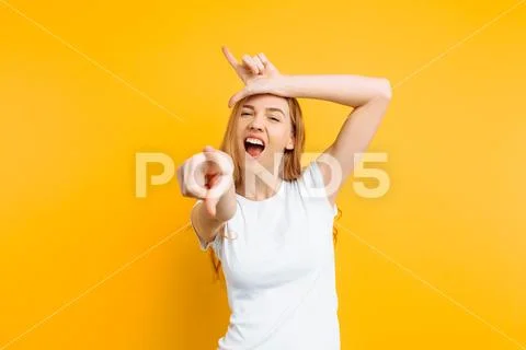 Girl shows the gesture of a loser or loser, in a white t-shirt with a grin on Stock Photos