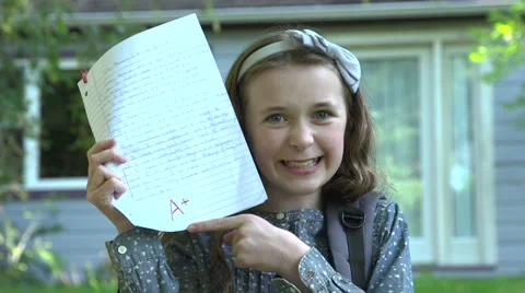 A girl shows off her A+ mark for her homework in front of her home. Stock Footage 44101853