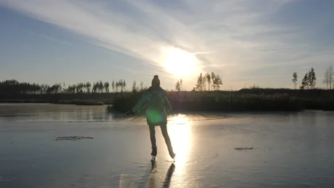 Girl in silver acket and backpack is skating along frozen lake to meet the sun Stock-Footage 145163061