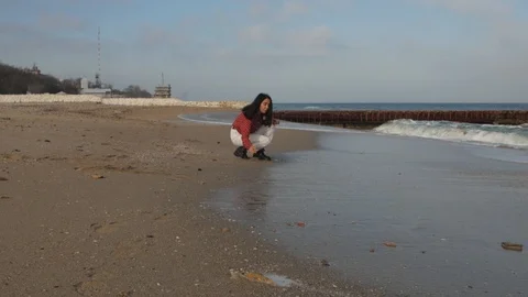 Girl sits on the beach and throws stones at sea against the sky Stock Footage 102016182