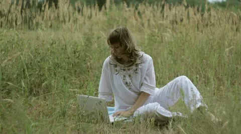 A girl sits on a field with a computer Stock Footage 12411810