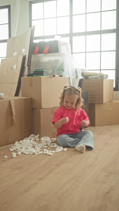 Girl sits on floor using hands to sort packing peanuts beside stacked cardb.. Stock Footage 339259897