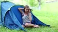 Girl sits on grass near tourist tent and speaks on cell phone HD Footage