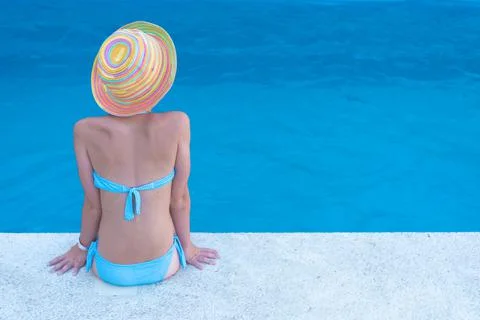 The girl sits with her back to the camera at the edge of the pool. The blue Stock Photos