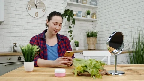 Girl sits at kitchen table texts message on phone smiling Stock Footage 101228874