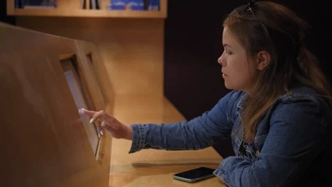 A girl sits in the library in front of a computer screen on the wall and studies Stock Footage 311153934