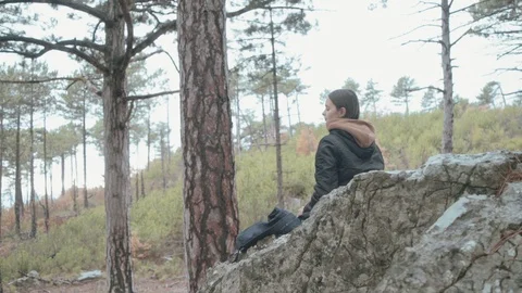 Girl sits on rock in the forest, resting and drinking hot coffee. 4K video Stock Footage 123364553