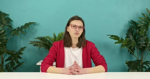 The girl sits at a table against a background of green plants. Stock Footage 159157428