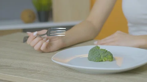 The girl sits at a table and eats broccoli adheres to a diet Stock Footage 128644873