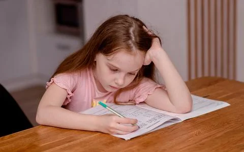 The girl sits at the table and solves problems, does her homework. School theme Stock Photos